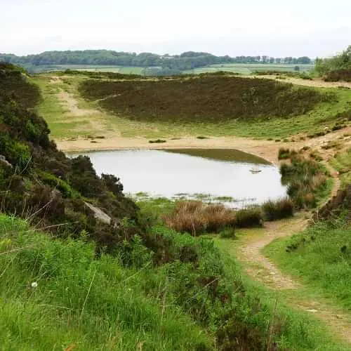 This image shows Penistone Hill pond which is surrounded by green hills and a pathway leading down to the pond