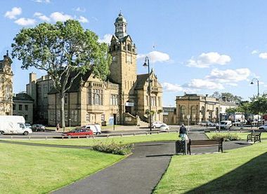Exterior of a town hall surrounded by grass with a paved pathway up to the building